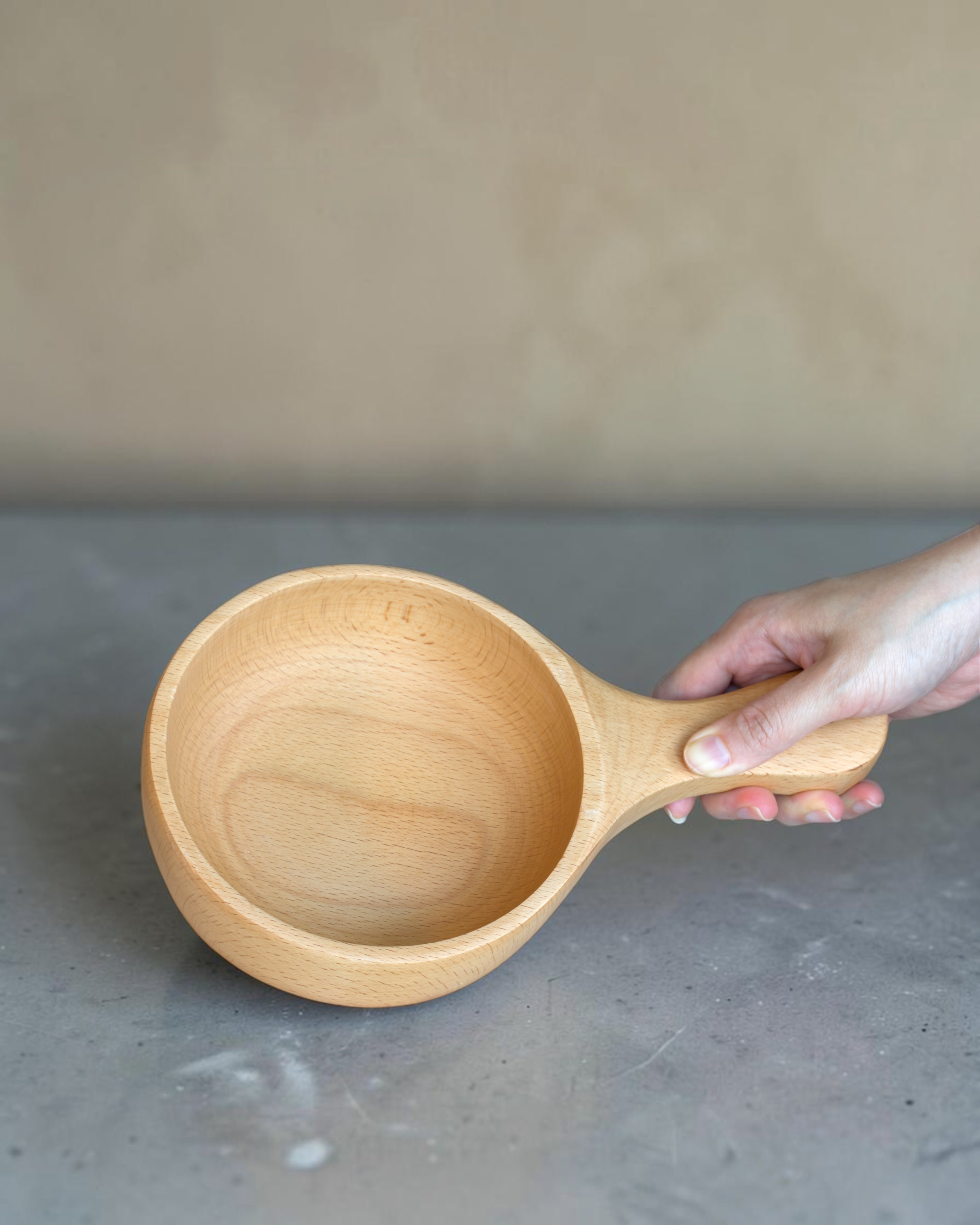 Ecohub NZ Entertainers Beech Handled Snack Bowl (15cm) - natural beech wood - being held by the handle over a grey concrete surface