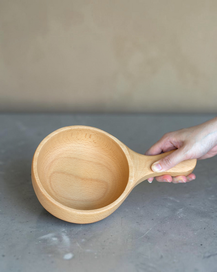 Ecohub NZ Entertainers Beech Handled Snack Bowl (15cm) - natural beech wood - being held by the handle over a grey concrete surface