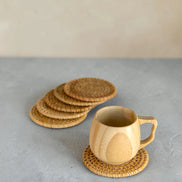 Ecohub NZ Artisans Rattan Coaster Set of 6 - natural woven rattan - one under a mug with others fanned out on concrete