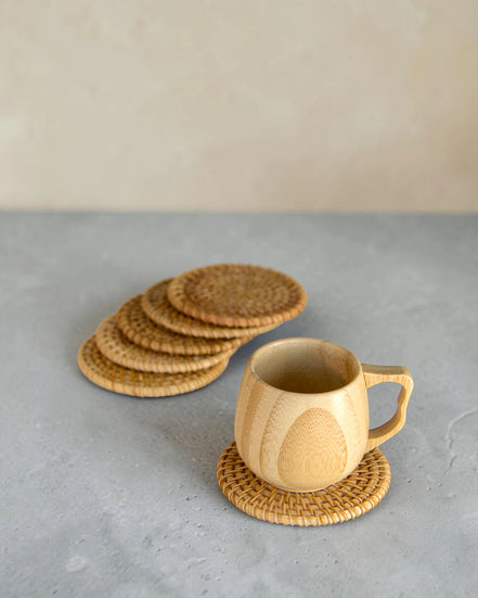 Ecohub NZ Artisans Rattan Coaster Set of 6 - natural woven rattan - one under a mug with others fanned out on concrete