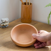 Ecohub NZ Entertainers Beech Nesting Bowl Set of 2 - natural beech wood - a hand holding one bowl over a sunlit wood counter