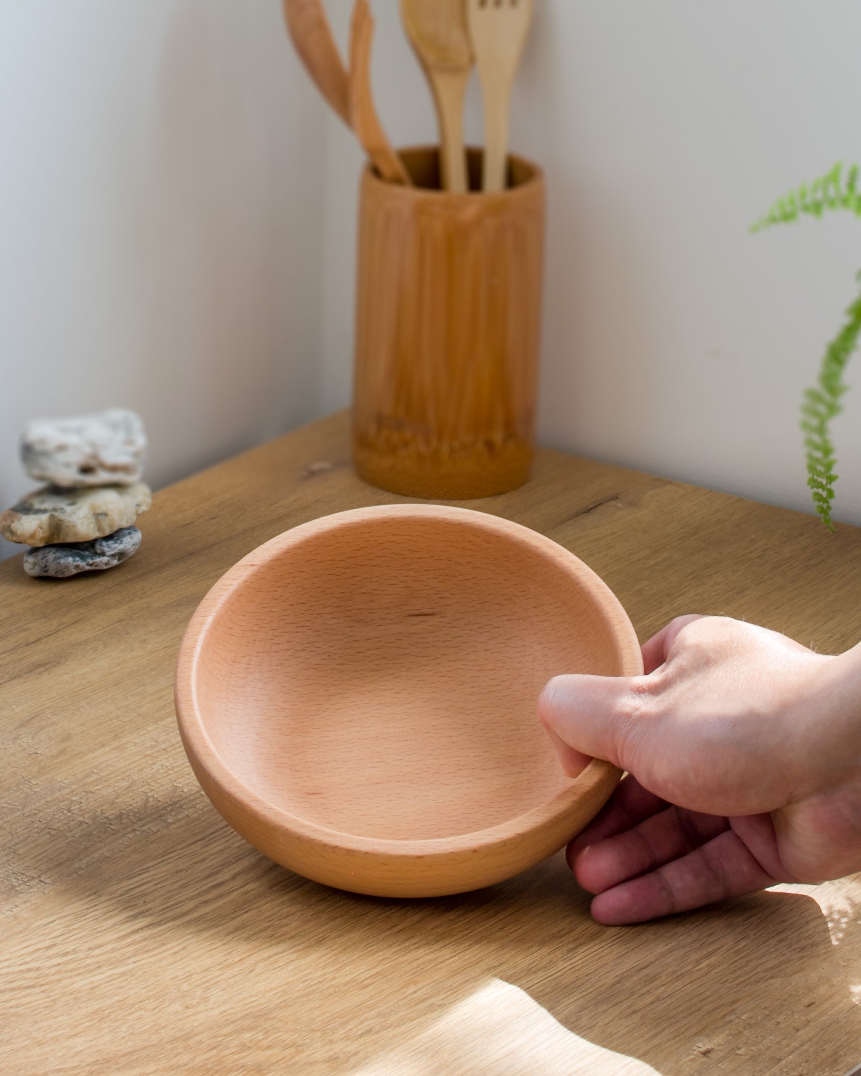 Ecohub NZ Entertainers Beech Nesting Bowl Set of 2 - natural beech wood - a hand holding one bowl over a sunlit wood counter