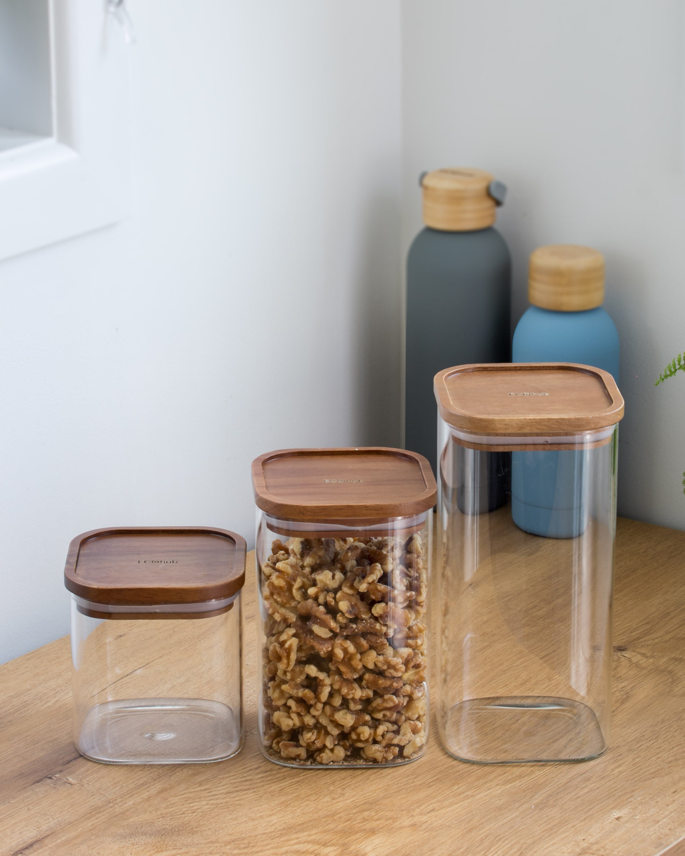 Ecohub NZ Essentials Square Acacia & Glass Pantry Jar (1.2L) - glass and acacia - holding nuts on a wood counter